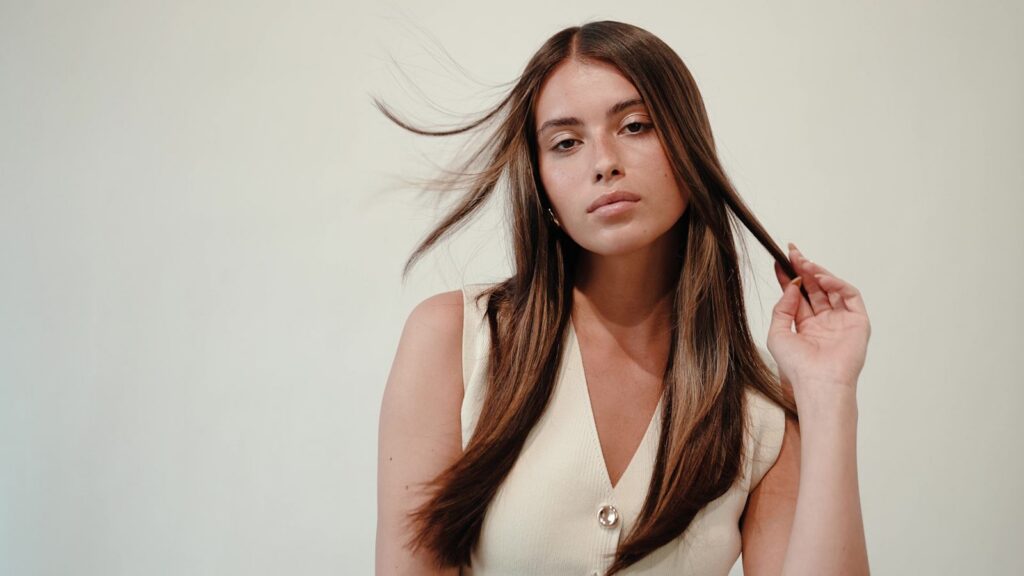 Vrouw met lang, steil bruin haar speelt met een lok haar
